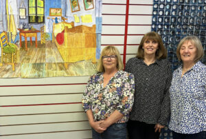 3 women standing next to a pastel artwork